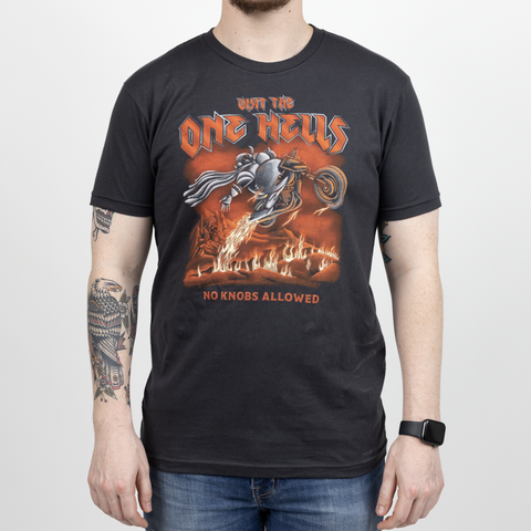 Male model in graphite black shirt with graphic of motor cycle going through flames with text "VISIT THE ONE HELLS NO KNOBS ALLOWED"